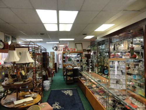 A cozy antique shop filled with various collectibles, display cases, and decorative items under bright ceiling lights.