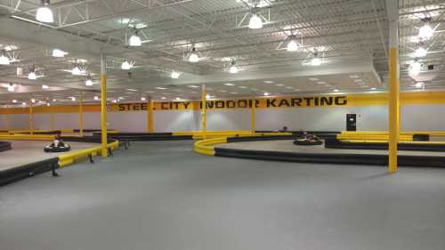 Indoor karting track with yellow and black barriers, featuring a spacious layout and the words "Steel City Indoor Karting" on the wall.