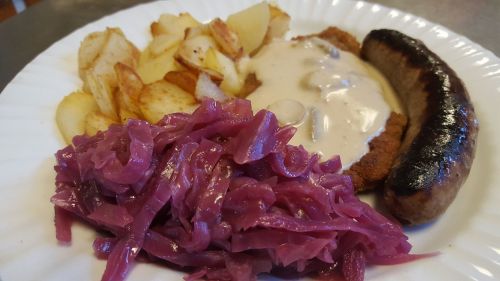 A plate of food featuring fried potatoes, sausage, schnitzel with gravy, and purple cabbage.