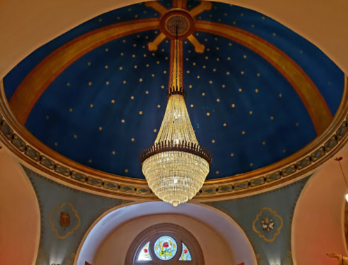 A grand chandelier hangs from a blue ceiling adorned with gold stars and decorative patterns.