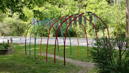 Colorful archway structure in a green park, with trees and a road visible in the background.