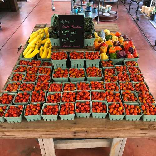 A vibrant display of fresh produce, featuring baskets of cherry tomatoes, peppers, and bananas on a wooden table.