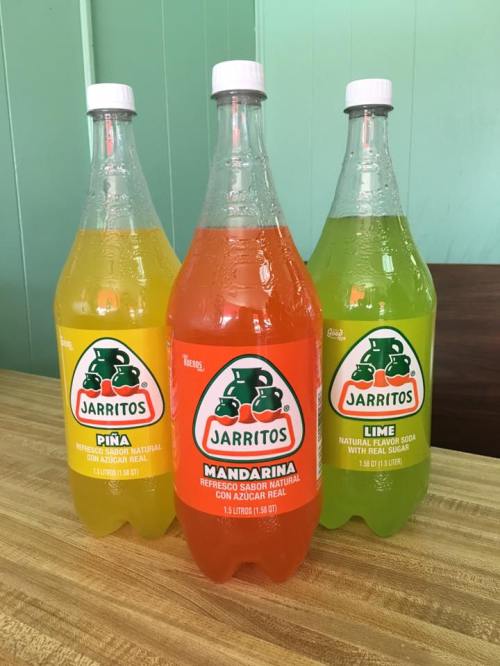 Three bottles of Jarritos soda in flavors: Piña (yellow), Mandarina (orange), and Lime (green) on a wooden table.