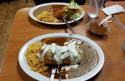 Two plates of Mexican food featuring burritos topped with sauce, rice, beans, and garnished with lettuce and sour cream.