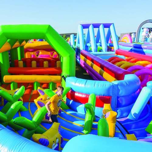 A colorful inflatable obstacle course with various structures and a person navigating through it under a clear blue sky.
