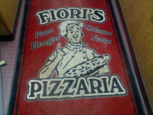 A red mat featuring the logo of Fiori's Pizzaria, depicting a chef holding a pizza and text for pizza, hoagies, calzone, and pasta.
