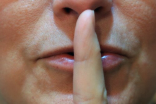 Close-up of a person's face with a finger held to their lips, signaling for silence.