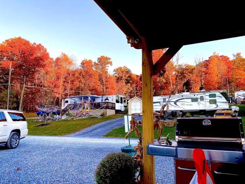 A scenic view of RVs parked among vibrant autumn trees, with a grill in the foreground and a clear blue sky.