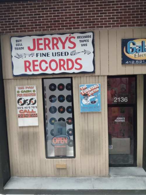 A storefront with a sign reading "Jerry's Records," featuring vinyl records and a welcoming "Open" sign.
