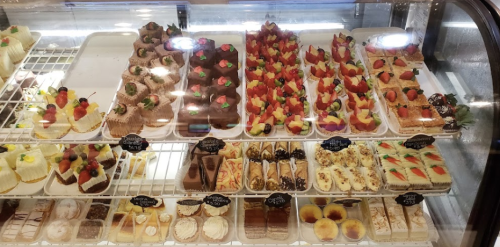 A display case filled with various colorful desserts, including cakes, pastries, and fruit-topped treats.
