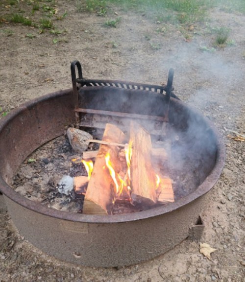 A fire burning in a circular metal fire pit, with smoke rising and logs crackling.