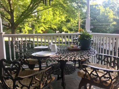 A cozy outdoor dining table set with plates and a plant, surrounded by green trees and a white railing.