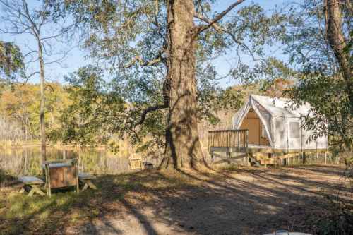 A glamping tent by a serene pond, surrounded by trees and autumn foliage.