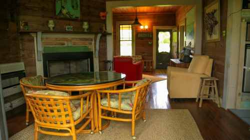Cozy interior of a rustic room featuring a round table, wicker chairs, and a fireplace, with warm wooden accents.
