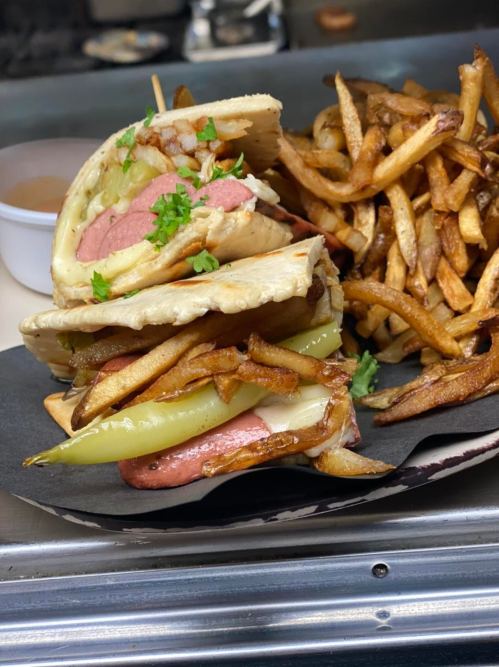 A sandwich filled with hot dog, pickles, and fries, served with a side of crispy French fries.