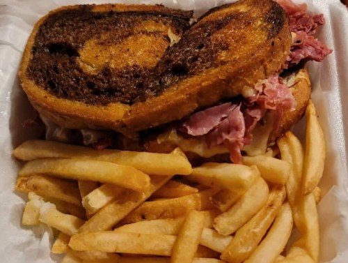 A grilled sandwich with layers of meat on toasted bread, served with a side of golden French fries.