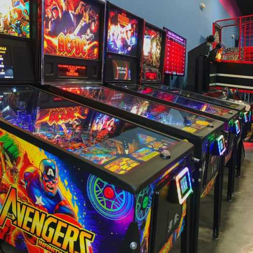 A row of colorful pinball machines featuring Avengers-themed graphics in a gaming arcade.