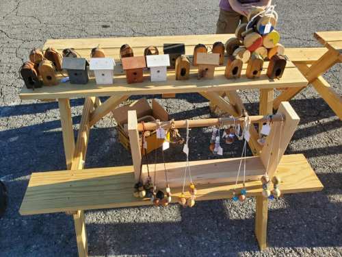 A wooden display table with various handcrafted wooden items, including small boxes and necklaces, in a market setting.