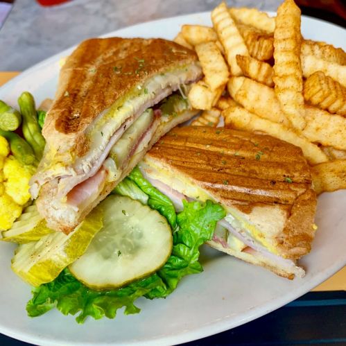 A toasted sandwich with ham, pickles, and lettuce, served with crispy crinkle-cut fries on the side.