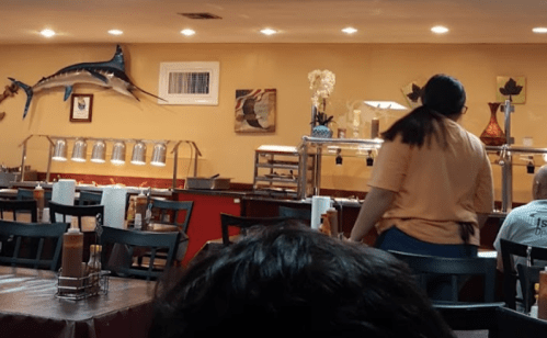 A restaurant interior with tables, a buffet setup, and a large marlin mounted on the wall. A server is walking by.