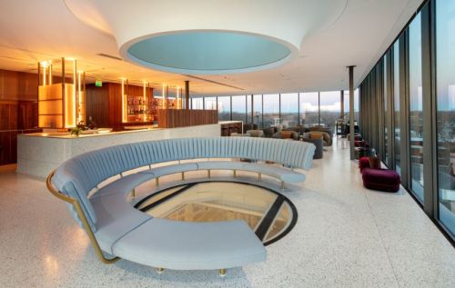 Modern lounge with a curved blue sofa, large windows, and a stylish bar area, featuring elegant lighting and decor.