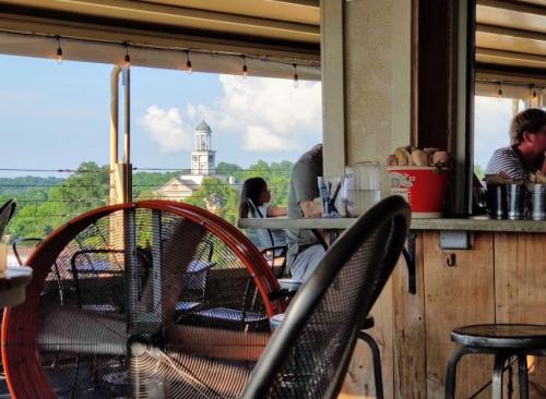 A view from inside a restaurant, featuring a fan, wooden decor, and a distant clock tower against a cloudy sky.