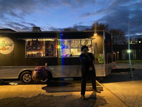 A food truck at dusk with colorful lights, featuring a person in costume standing in front, ready to serve.