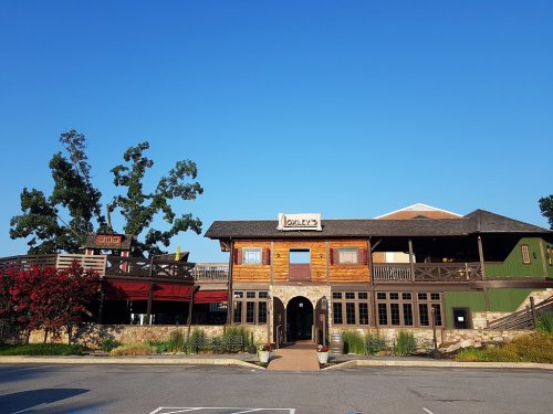 A rustic wooden restaurant with a sign reading "Oolly's," surrounded by greenery and a clear blue sky.