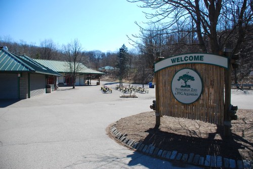 Welcome sign at the entrance of Pittsburgh Zoo & PPG Aquarium on a clear, sunny day with bare trees in the background.