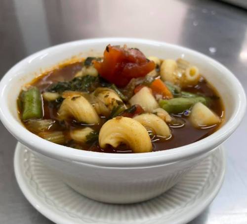 A bowl of hearty vegetable soup with pasta, featuring tomatoes, greens, and assorted vegetables.