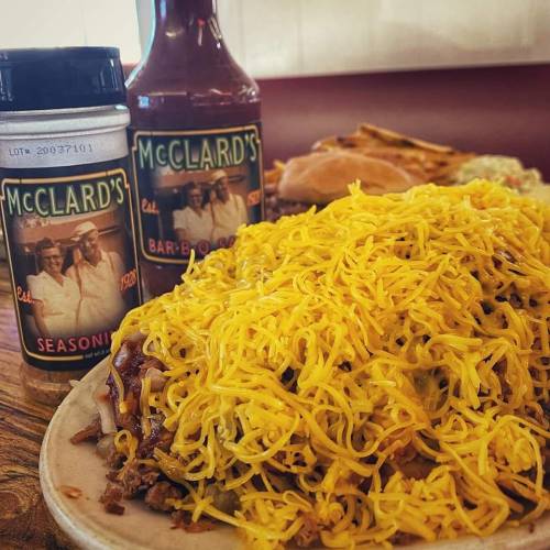A plate of shredded cheese over a meat dish, with McClard's seasoning and barbecue sauce in the background.