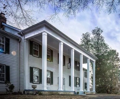 A historic white house with tall columns, surrounded by trees and a cloudy sky.
