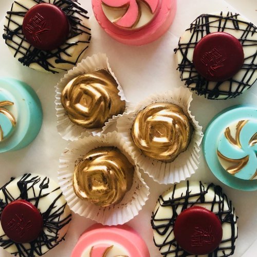 An assortment of decorative chocolates in various colors and designs, including gold, pink, and black patterns.