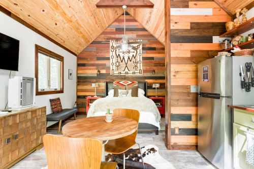 Cozy cabin interior featuring a wooden ceiling, a bed, dining table, and a kitchenette with rustic decor.