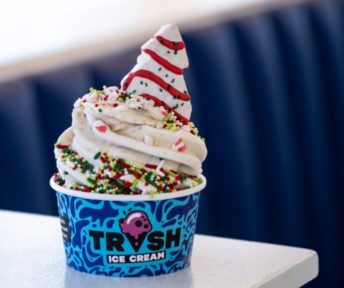 A festive ice cream cone topped with whipped cream, red and white stripes, and colorful sprinkles in a blue cup.