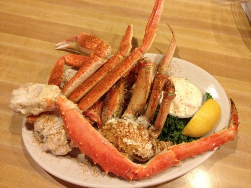 A plate of crab legs with seasoning, served with lemon and dipping sauce, garnished with lettuce.