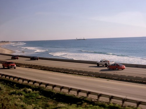 A scenic view of a highway alongside a beach, with cars driving and waves gently crashing on the shore.