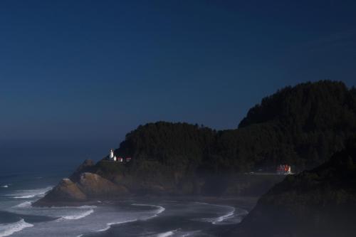 A coastal scene featuring a lighthouse on a rocky shore, surrounded by mist and waves under a dark blue sky.