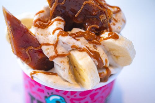 A close-up of a dessert cup filled with creamy ice cream, banana slices, and drizzled caramel sauce.