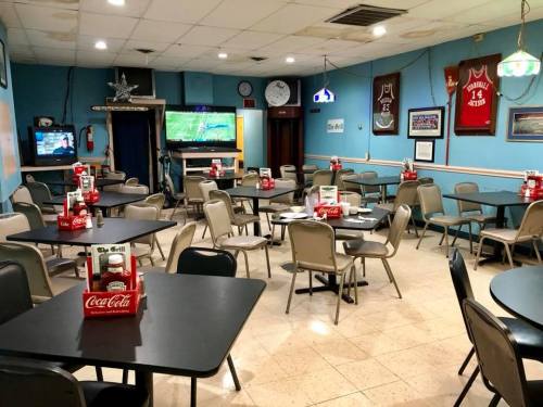 A casual dining area with empty tables, Coca-Cola boxes, and sports memorabilia on the walls. Two TVs are visible.
