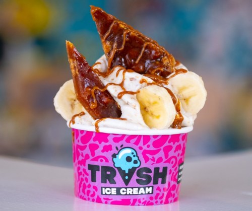 A colorful ice cream cup topped with caramel, banana slices, and crispy caramelized pieces.