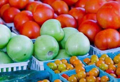 A colorful display of fresh tomatoes, green apples, and small orange fruits in baskets at a market.