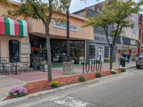 A street view of a small town featuring shops, a restaurant with an "Open" sign, and colorful flower beds.