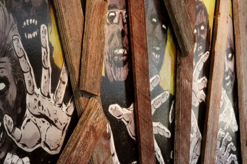 A close-up of a mural featuring zombie faces and hands, partially obscured by wooden planks.