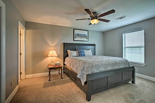 Cozy bedroom featuring a queen bed, nightstand, lamp, and ceiling fan, with light gray walls and a window.