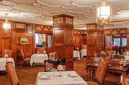 Elegant restaurant interior featuring wooden paneling, ornate decor, and neatly set tables. Soft lighting creates a warm ambiance.