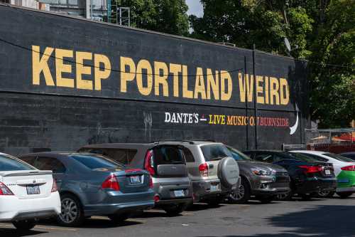 A mural reading "KEEP PORTLAND WEIRD" on a building, with parked cars in front.