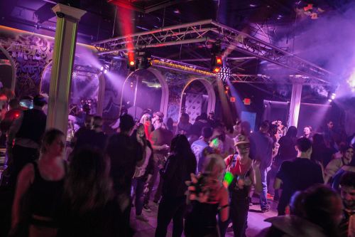 A lively dance party scene with people dancing under colorful lights and fog in a vibrant club atmosphere.