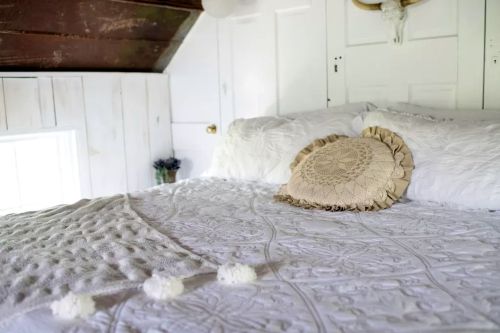 Cozy bedroom with a white quilted bedspread, decorative pillow, and soft lighting from a nearby window.