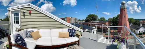 Rooftop view featuring a cozy seating area and a lighthouse in the background under a bright blue sky.